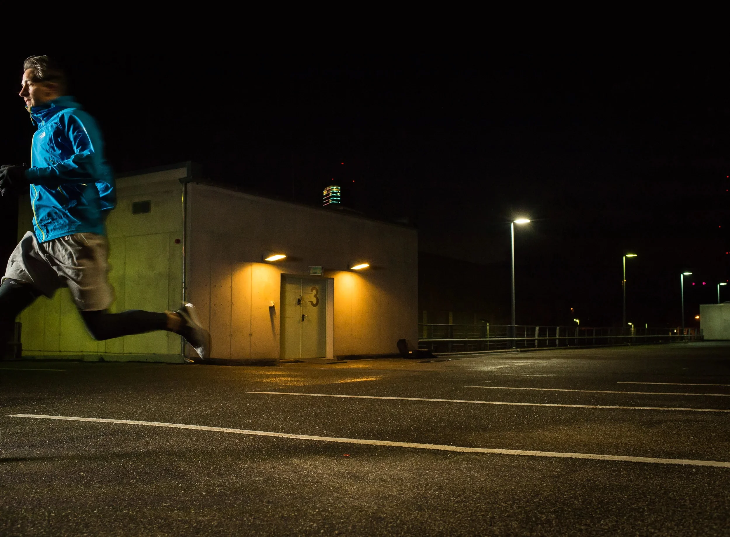 Night action shot of a runner passing a building, with motion blur and streetlights.
